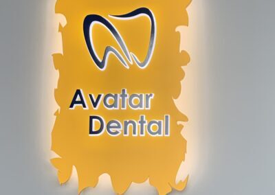 Illuminated Avatar Dental logo sign mounted on a gray wall, featuring a stylized tooth graphic on a bright orange background