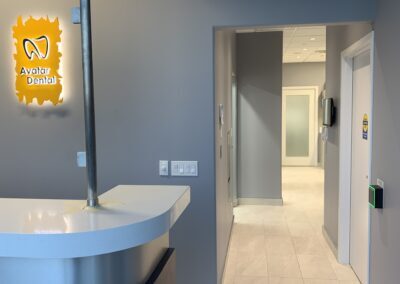 Interior hallway view at Avatar Dental showing a curved reception counter, wall-mounted clinic logo, and well-lit corridor leading to treatment rooms