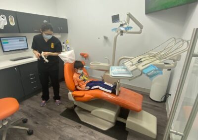 Child sitting in an orange dental chair during a checkup at Avatar Dental, with a dental assistant standing nearby in black scrubs