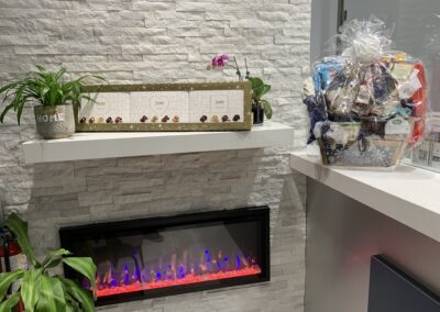 Reception area at Avatar Dental featuring a modern electric fireplace, decorative plants, a gift basket, and a “Welcome” sign
