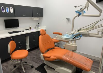 Modern dental operatory at Avatar Dental featuring an orange dental chair, matching stool, computer workstation, and overhead dental equipment