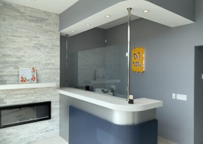 Modern dental clinic reception desk with a curved countertop, clear protective screen, and a stone accent wall with an electric fireplace