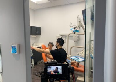 Filming inside a dental operatory at Avatar Dental, capturing a staff member interacting with a patient in an orange chair, with a video monitor showing the live feed