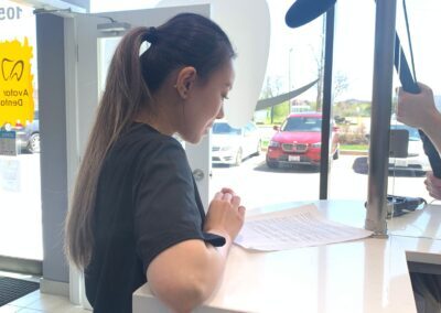 Avatar Dental staff member at the reception desk being recorded during a video shoot, with lighting and microphone equipment positioned nearby