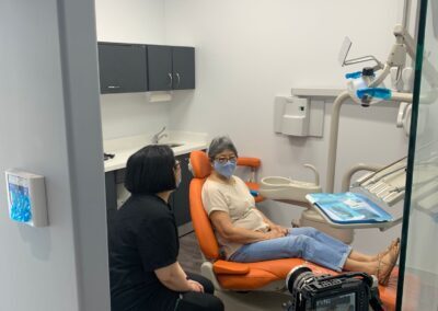 Patient seated in an orange dental chair at Avatar Dental while a staff member provides care, with a video crew capturing the interaction inside the treatment room